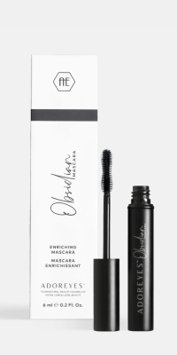 An open mascara tube displaying the unique application brush, sitting in front of the white retail box on a soft grey background